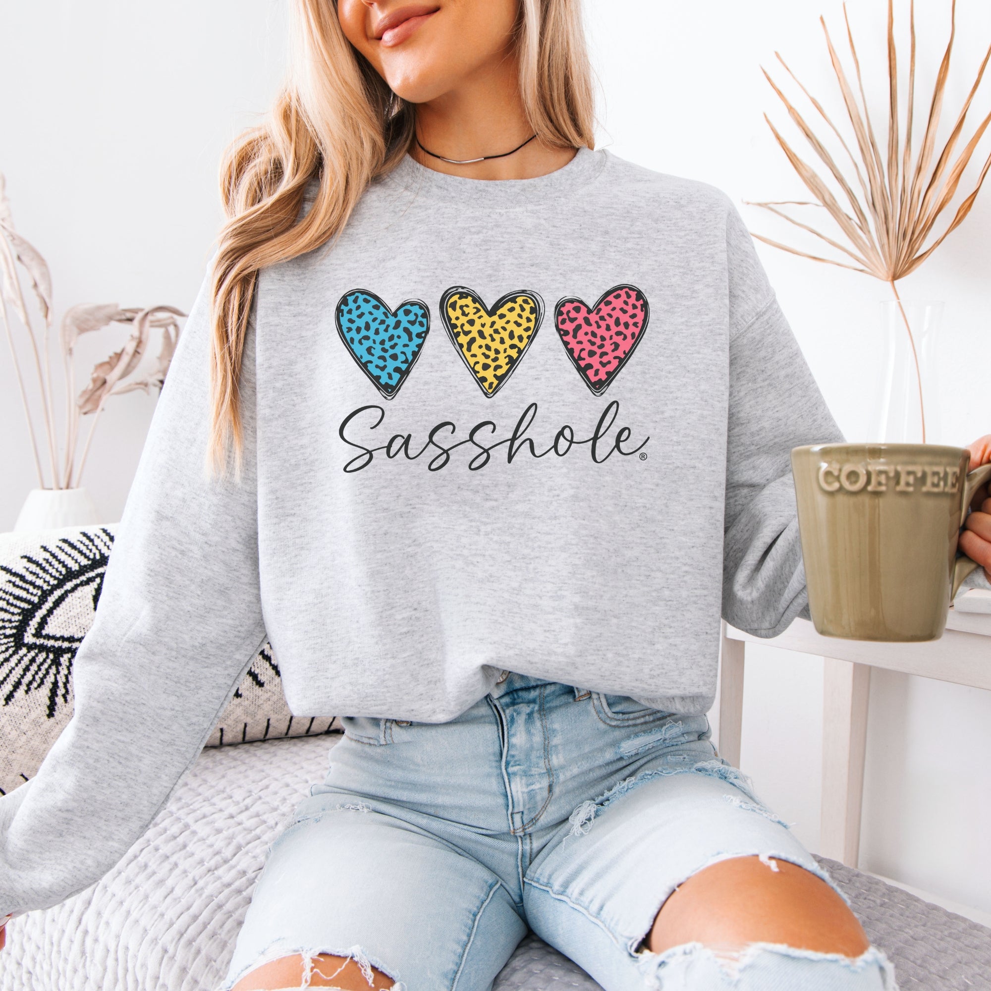 Image of Person wearing a gray sweatshirt with colorful heart designs and text, holding a mug.
