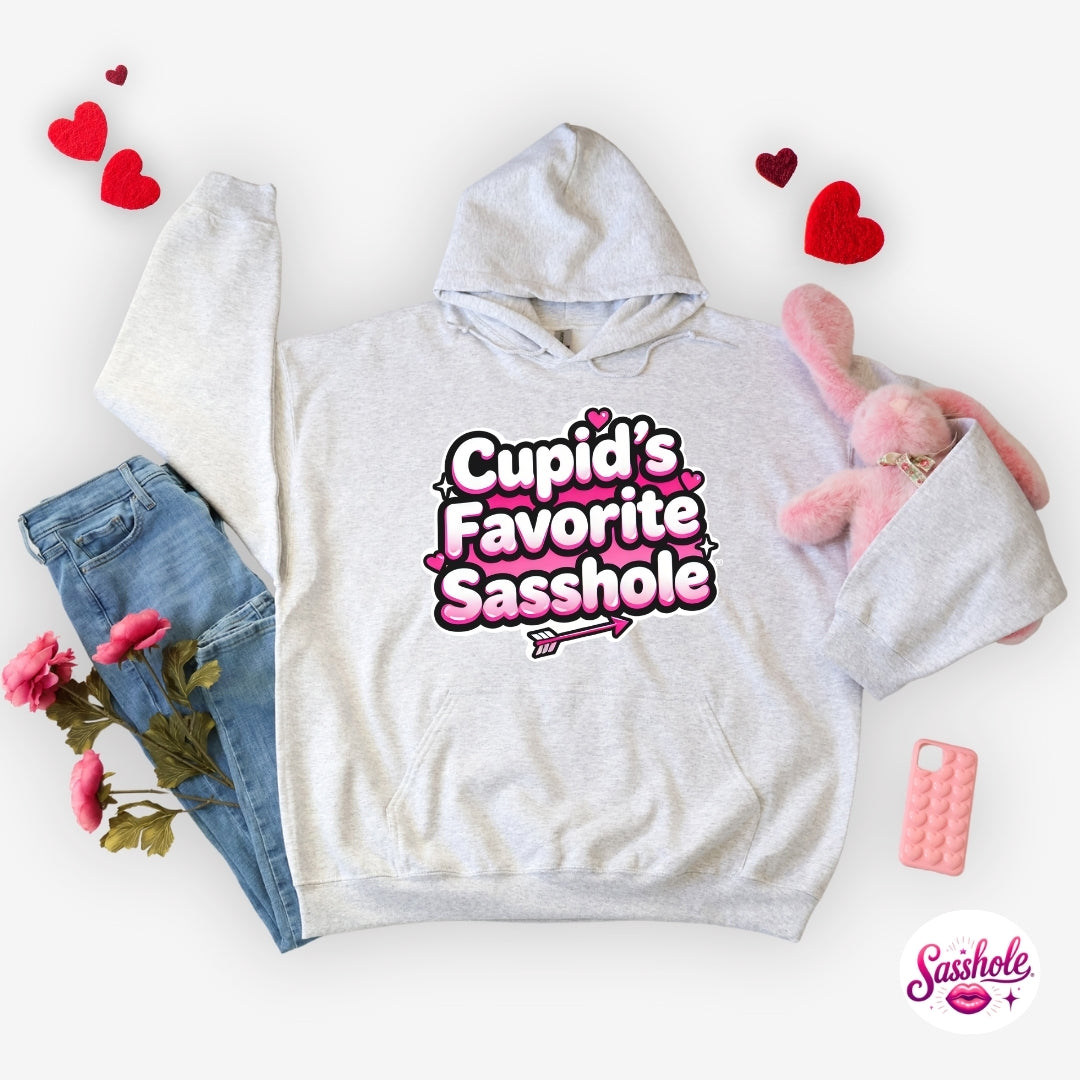 Image of Gray hoodie with 'Cupid's Favorite Sasshole' text, surrounded by jeans, flowers, and a phone on a white background.