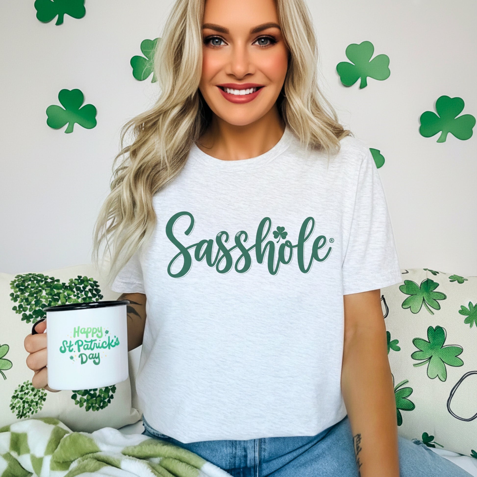 Woman wearing a white t-shirt with 'Sasshole' printed on it, holding a mug with St. Patrick's Day design.