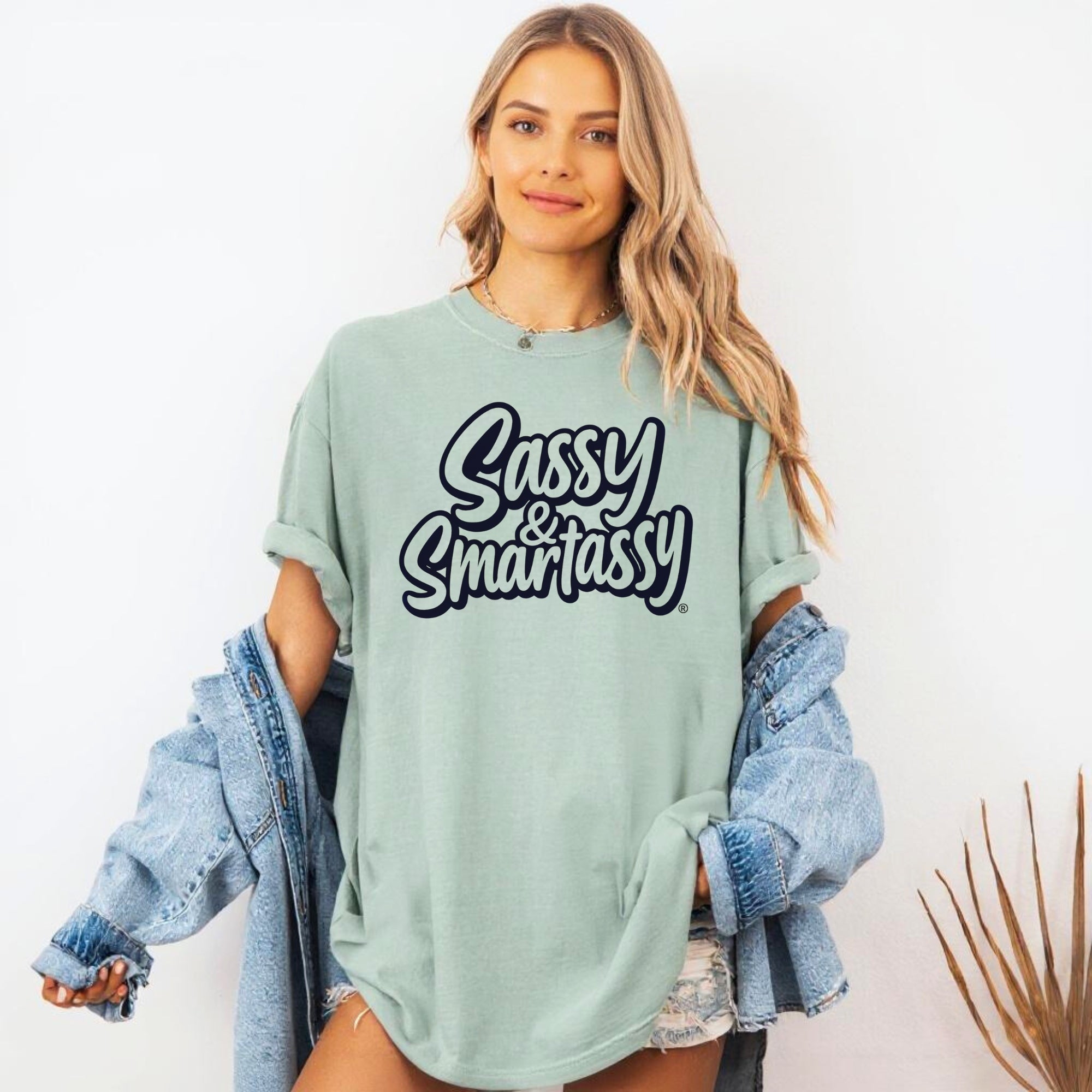 Image of Woman wearing a light green oversized t-shirt with 'Sassy & Smartassy' text, holding a denim jacket.