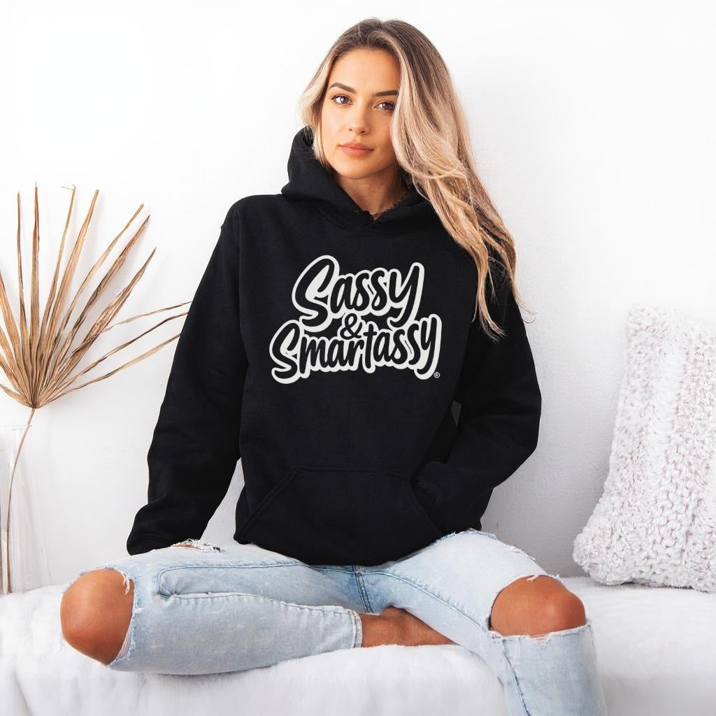 Image of Woman wearing a black hoodie with 'Sassy & Smartassy' text, sitting on a white couch.