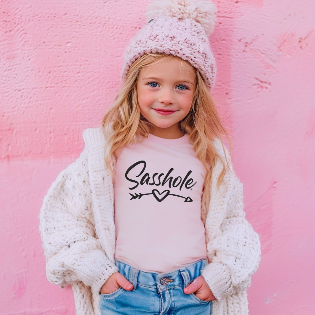 Image of Child wearing a pink shirt with 'Sasshole' text, white cardigan, and blue jeans against a pink background