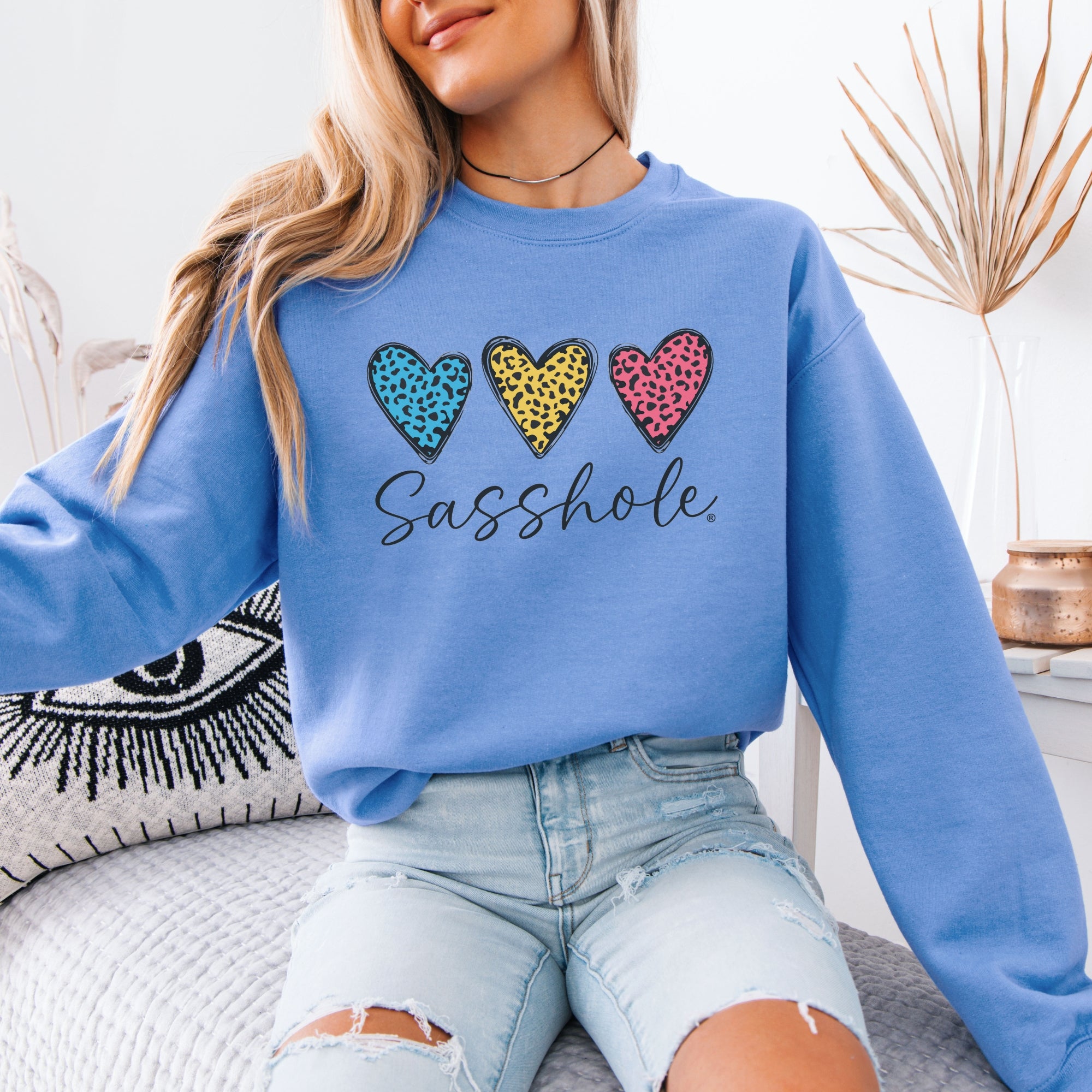 Image of Person wearing a blue sweatshirt with colorful heart designs and text, sitting on a couch.