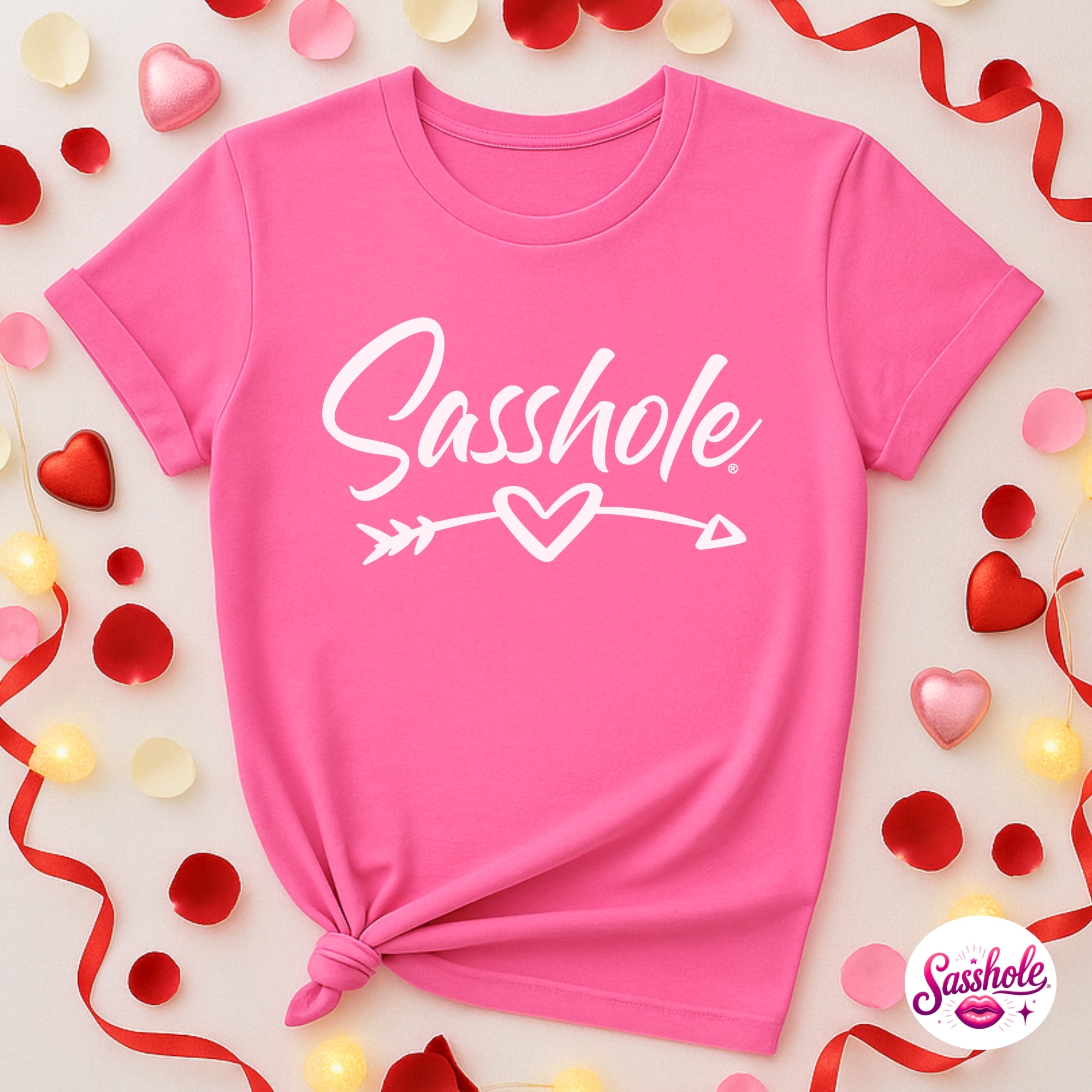 Pink t-shirt with 'Sasshole' text surrounded by decorative elements on a light background
