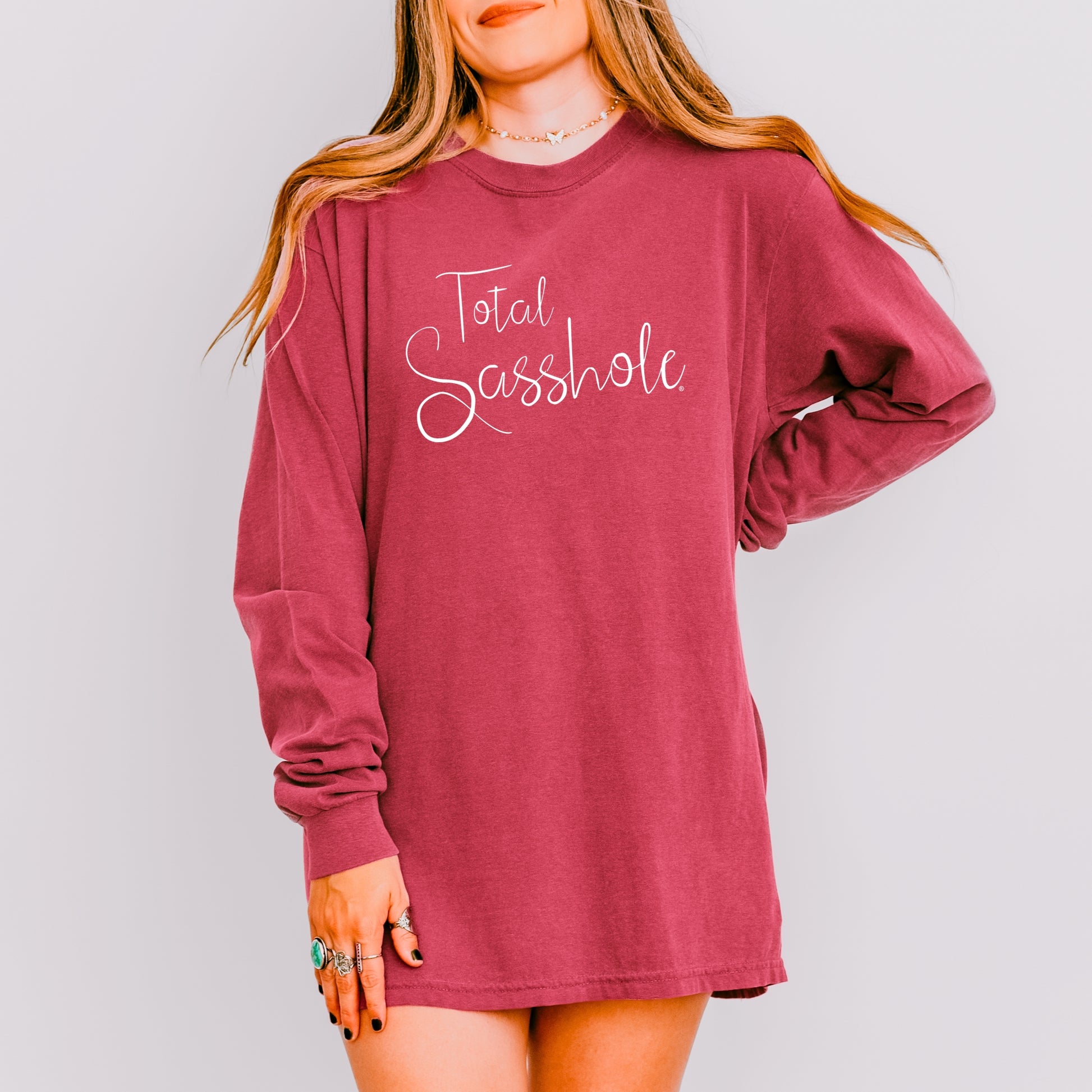 Crimson long-sleeve shirt with 'Total Sasshole' text worn by a woman on a gray background
