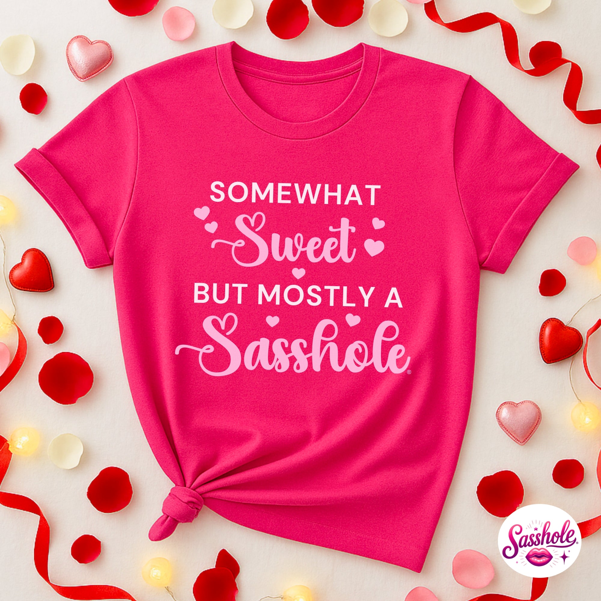 Pink t-shirt with humorous text surrounded by decorative hearts and ribbons on a light background
