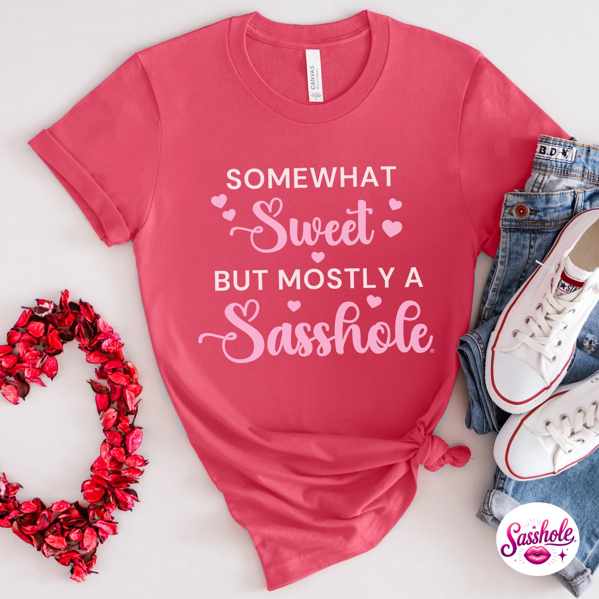 Image of Pink t-shirt with humorous text, surrounded by jeans, sneakers, and decorative heart on a light background