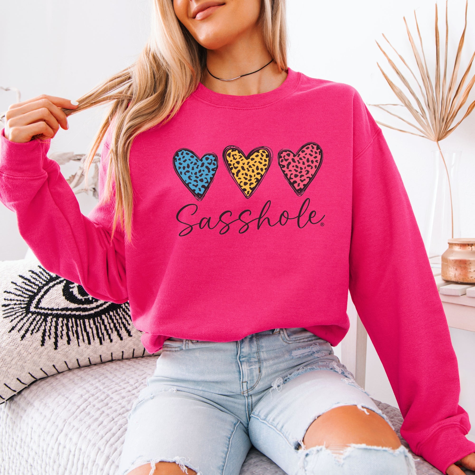 Image of Person wearing a pink sweatshirt with colorful heart designs and the word 'Sasshole'.