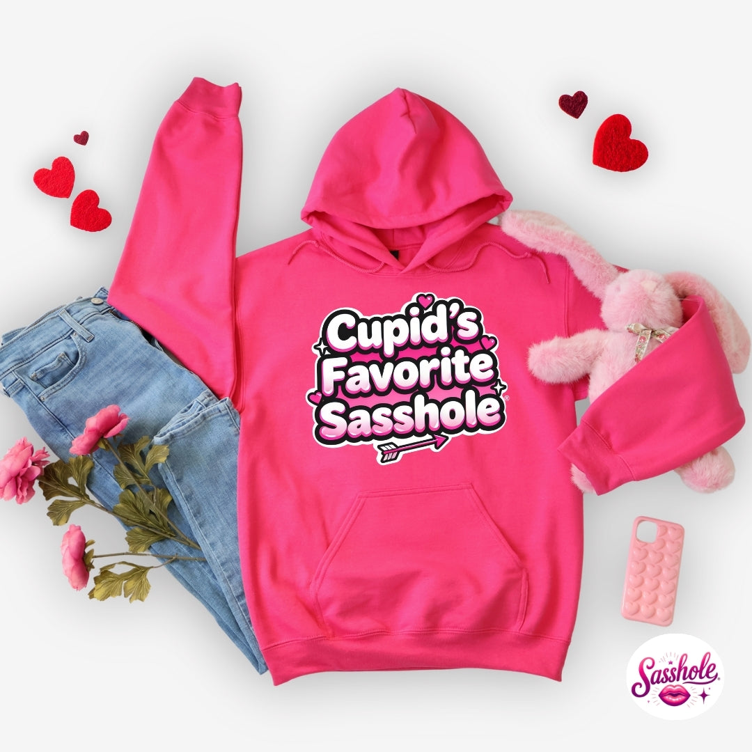 Pink hoodie with 'Cupid's Favorite Sasshole' text, denim shorts, flowers, and a pink plush toy on a white background.