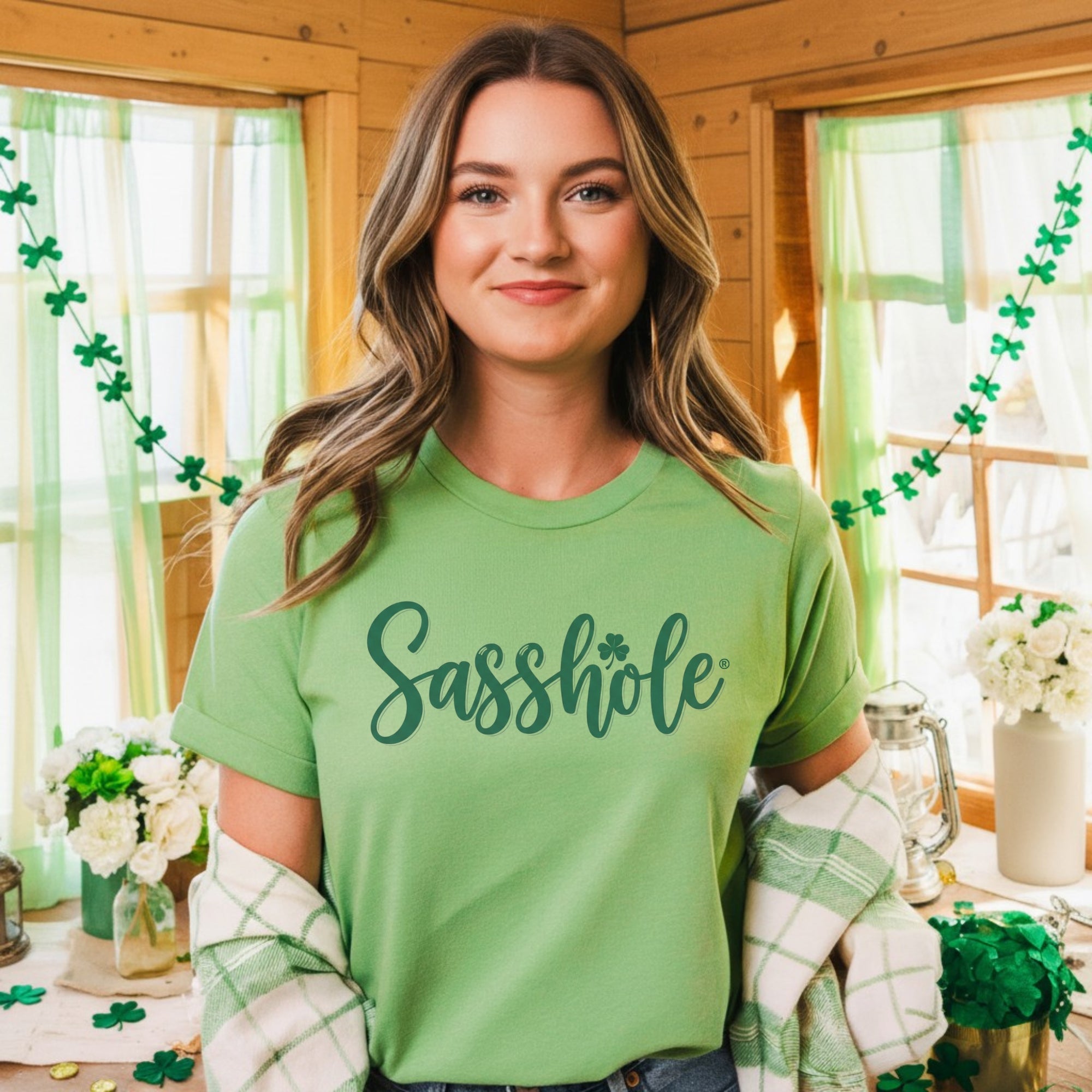 Image of Woman wearing a green t-shirt with 'Sasshole' printed on it, standing in a festively decorated room.