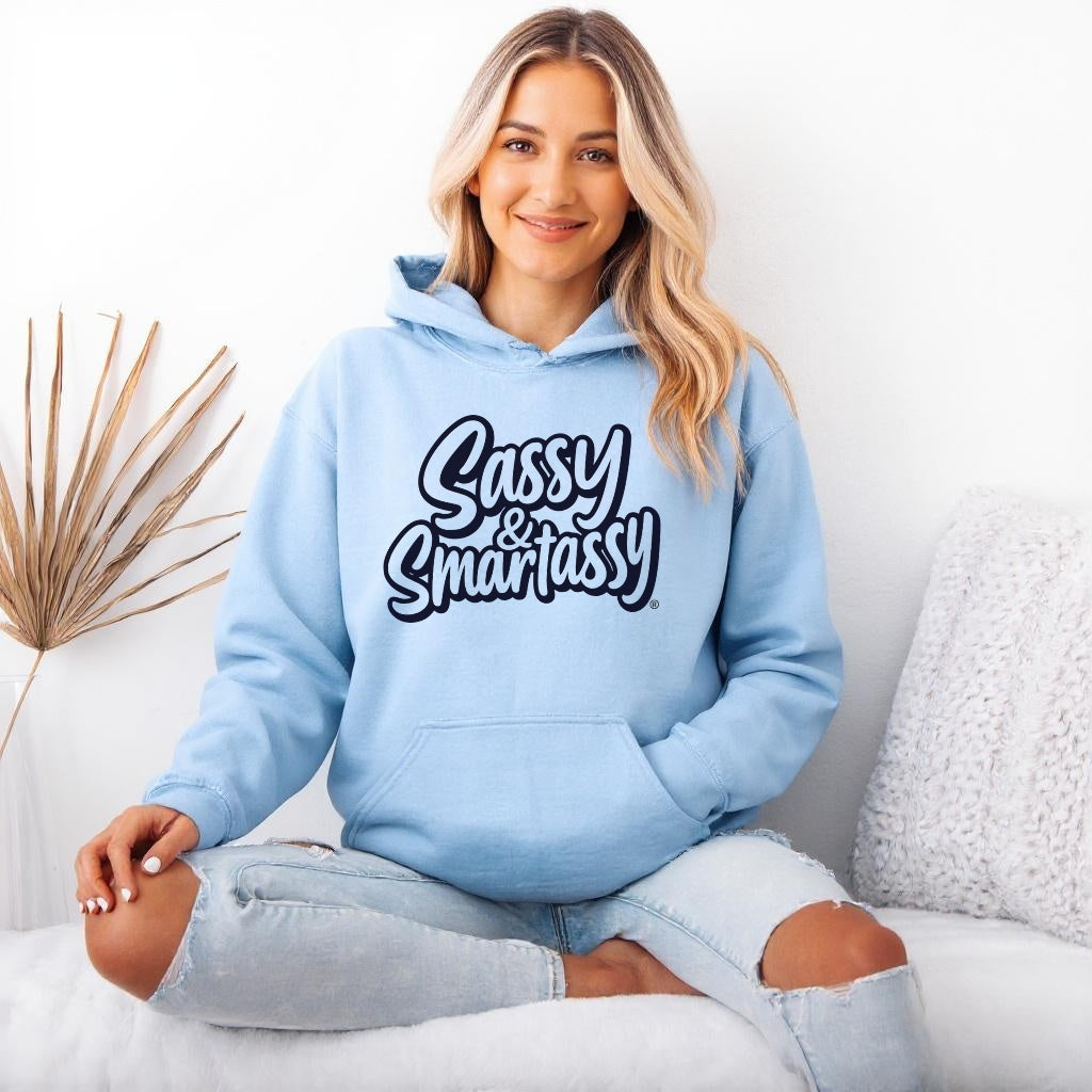 Woman wearing a light blue hoodie with 'Sassy & Smartassy' text, sitting on a white couch.
