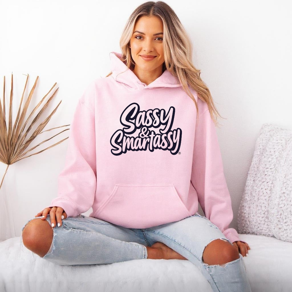 Woman wearing a light pink hoodie with 'Sassy & Smartassy' text, sitting on a couch.