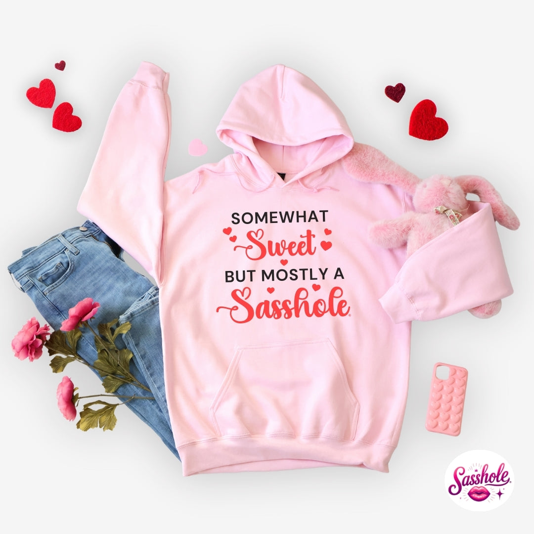 Pink hoodie with humorous text, surrounded by hearts, flowers, and a phone on a light background.