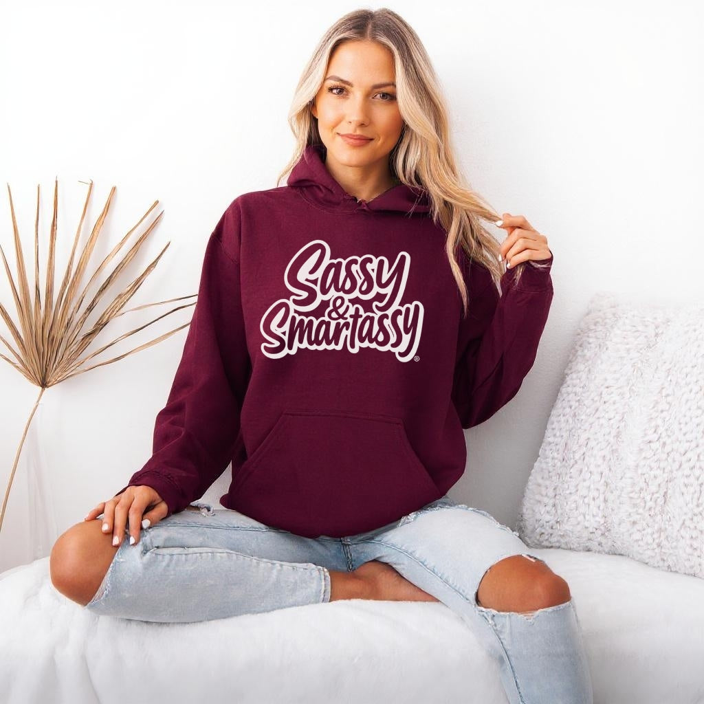 Woman wearing a maroon hoodie with 'Sassy & Smartassy' text, sitting on a white couch.