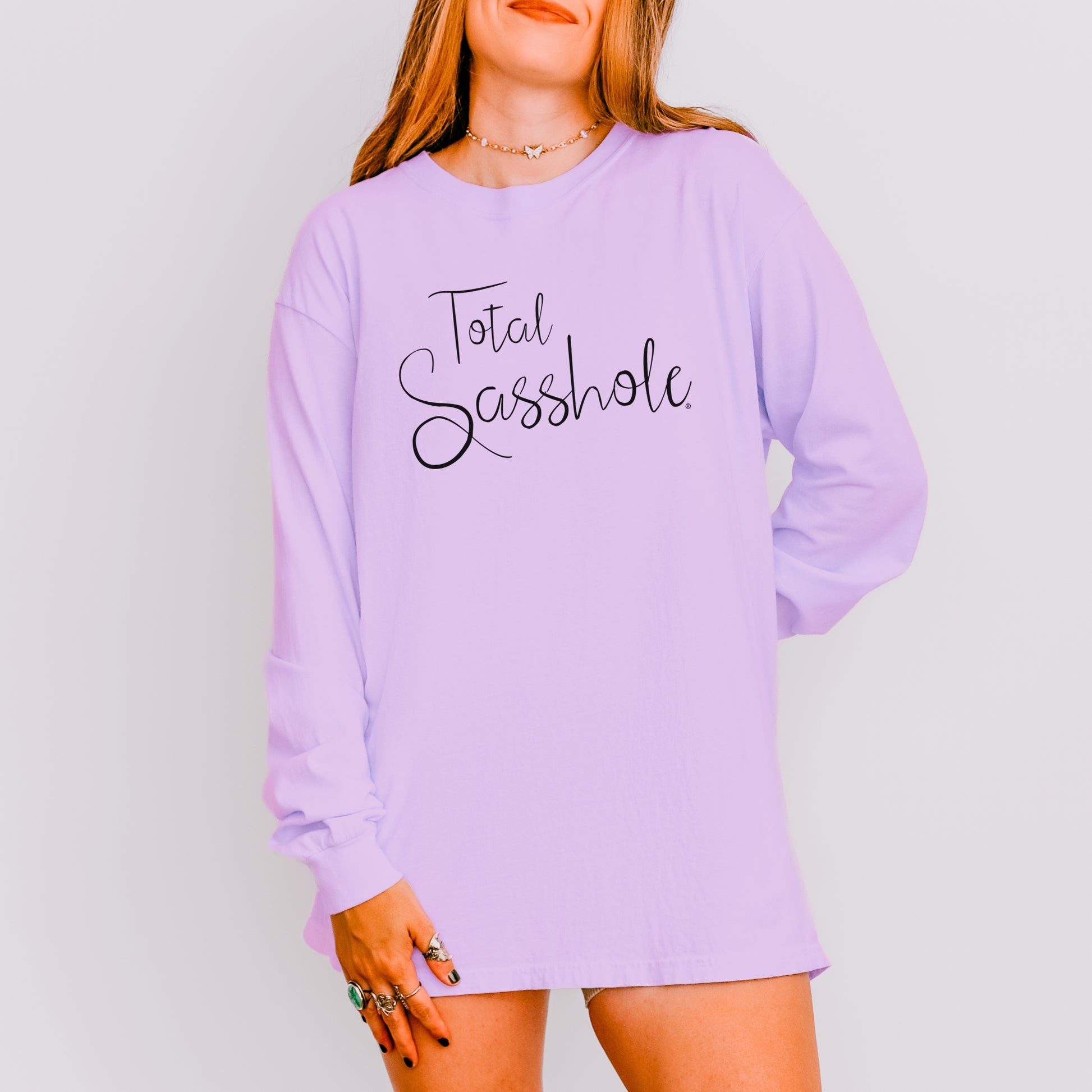 Woman wearing an orchid color long-sleeve shirt with 'Total Sasshole' text on a plain background