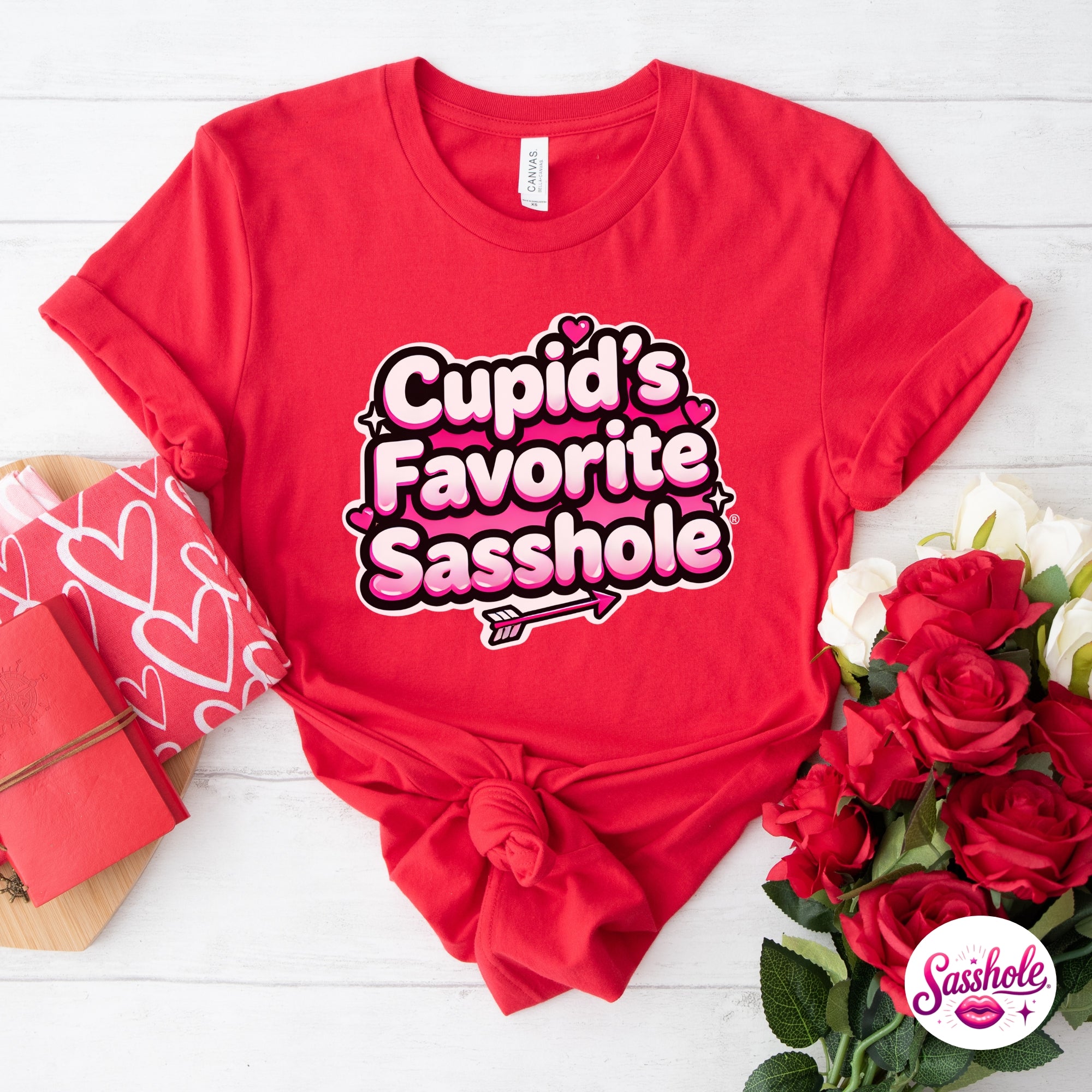 Red t-shirt with 'Cupid's Favorite Sasshole' text, surrounded by roses and gift boxes on a white background