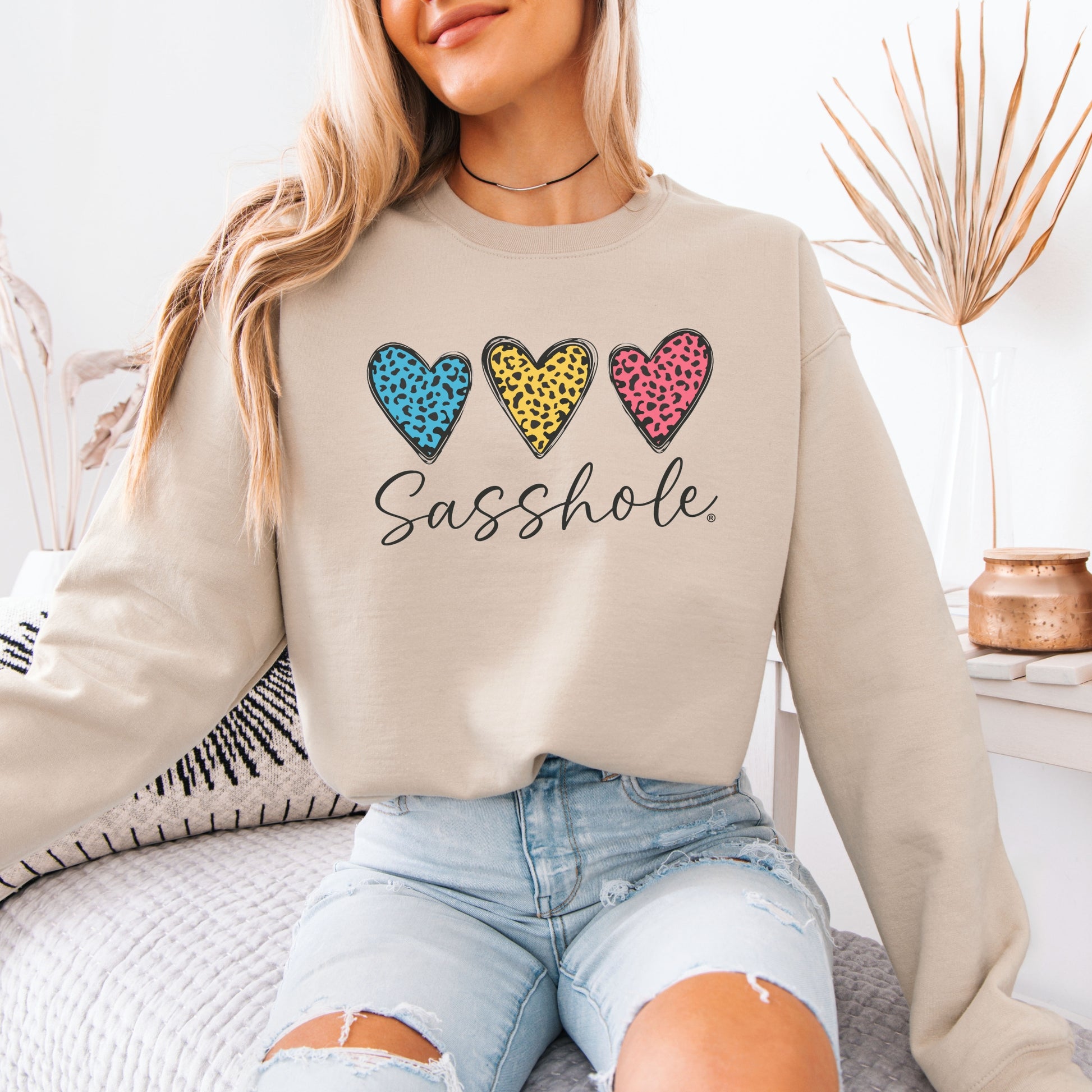 Person wearing a beige sweatshirt with colorful heart designs and the text 'Sasshole'.