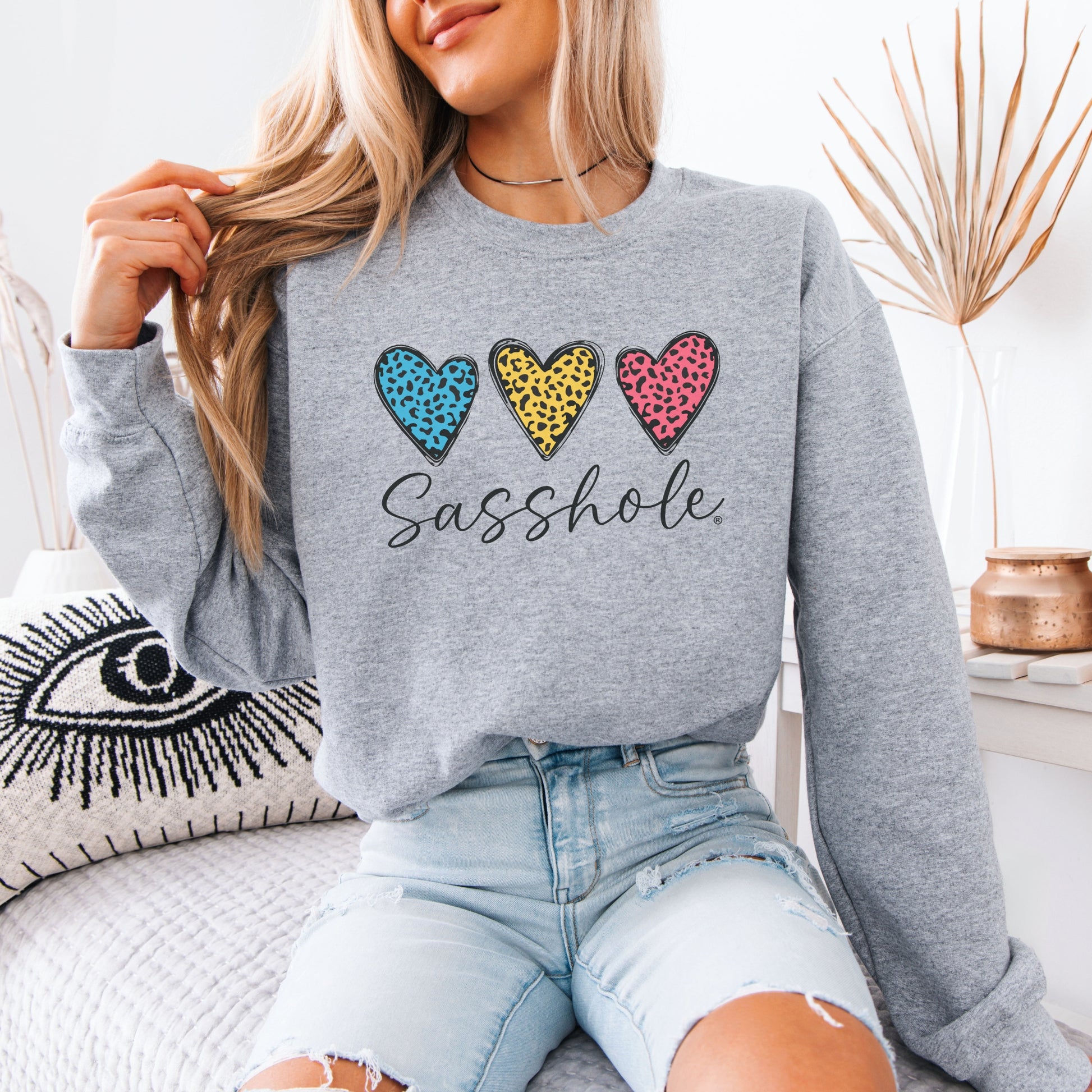 Person wearing a gray sweatshirt with colorful heart designs and text, sitting on a couch.