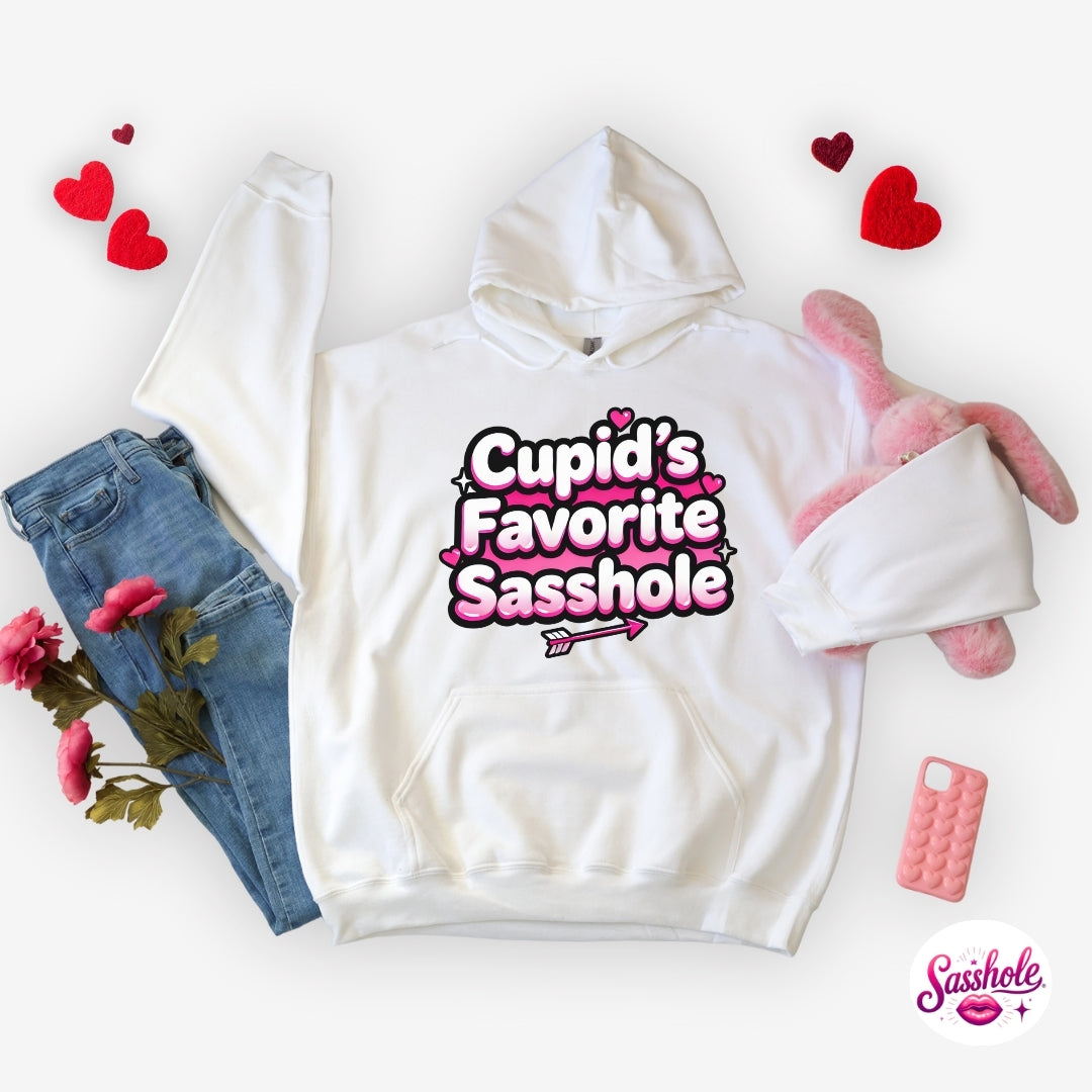 Image of White hoodie with 'Cupid's Favorite Sasshole' text, surrounded by jeans, flowers, and a pink plush toy on a white background.