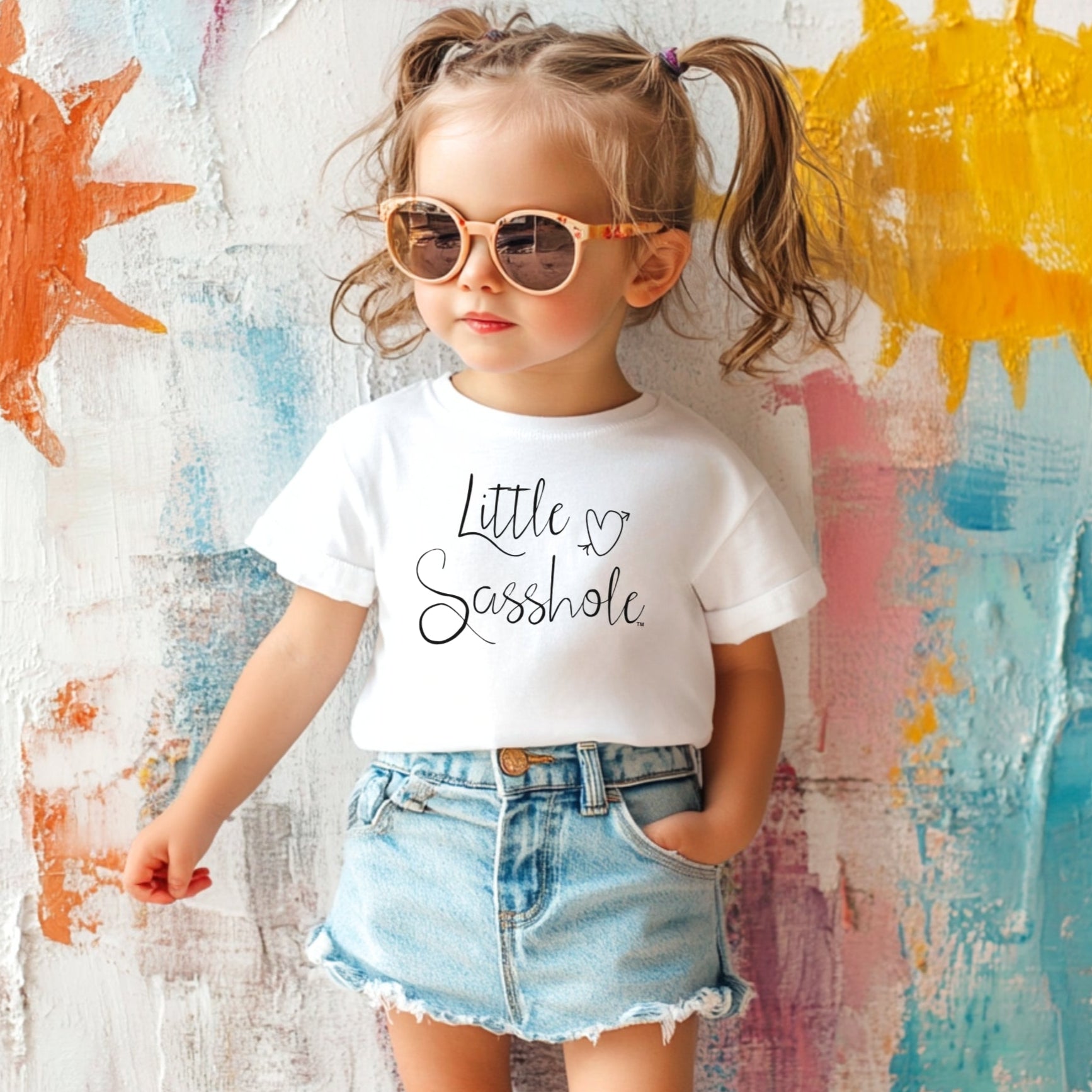 Child wearing a white t-shirt with text and denim shorts against a colorful abstract background