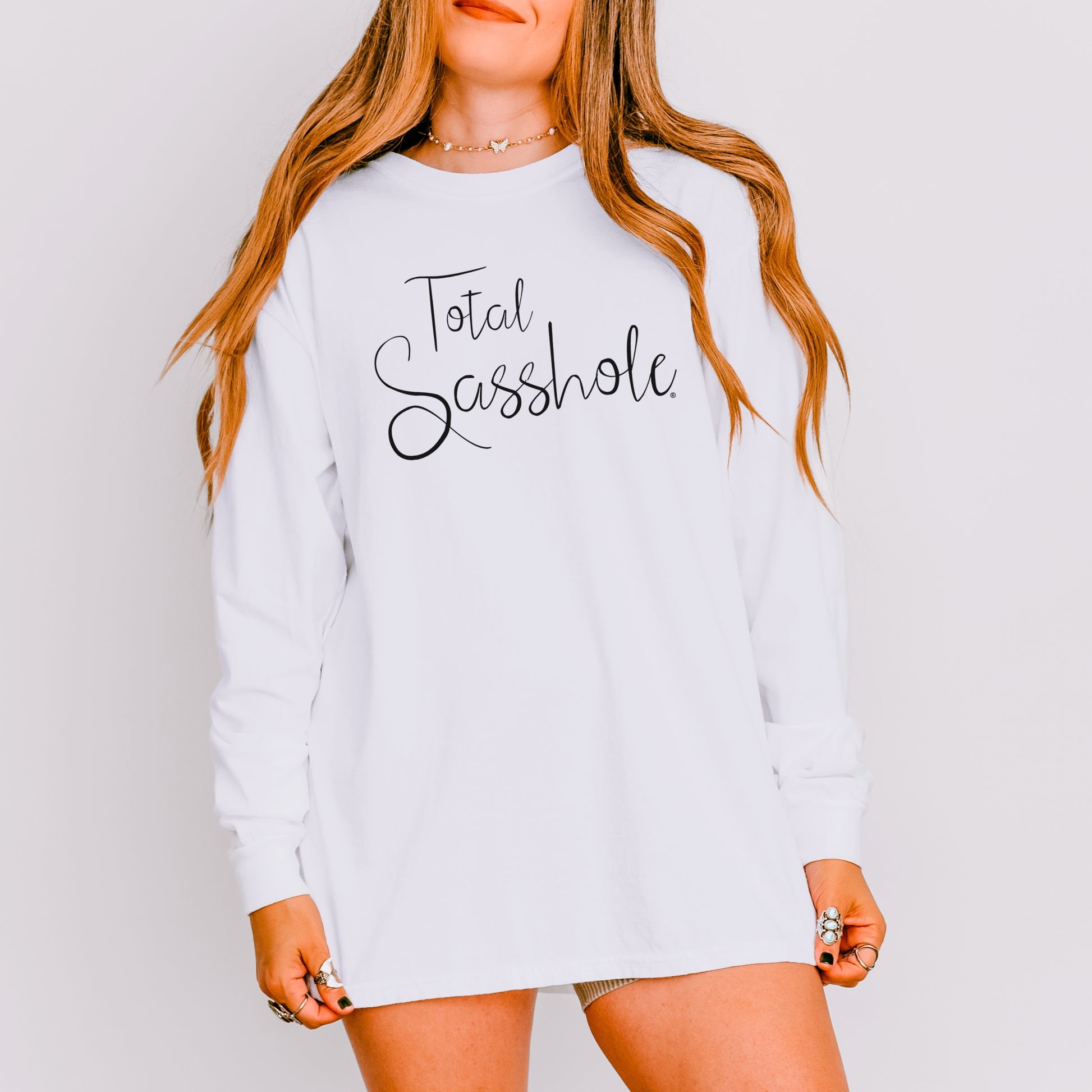 Woman wearing a white long sleeve t-shirt with 'Total Sasshole' text on a plain background