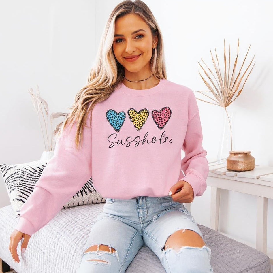 Woman wearing a pink sweatshirt with colorful heart designs and text, sitting on a couch.