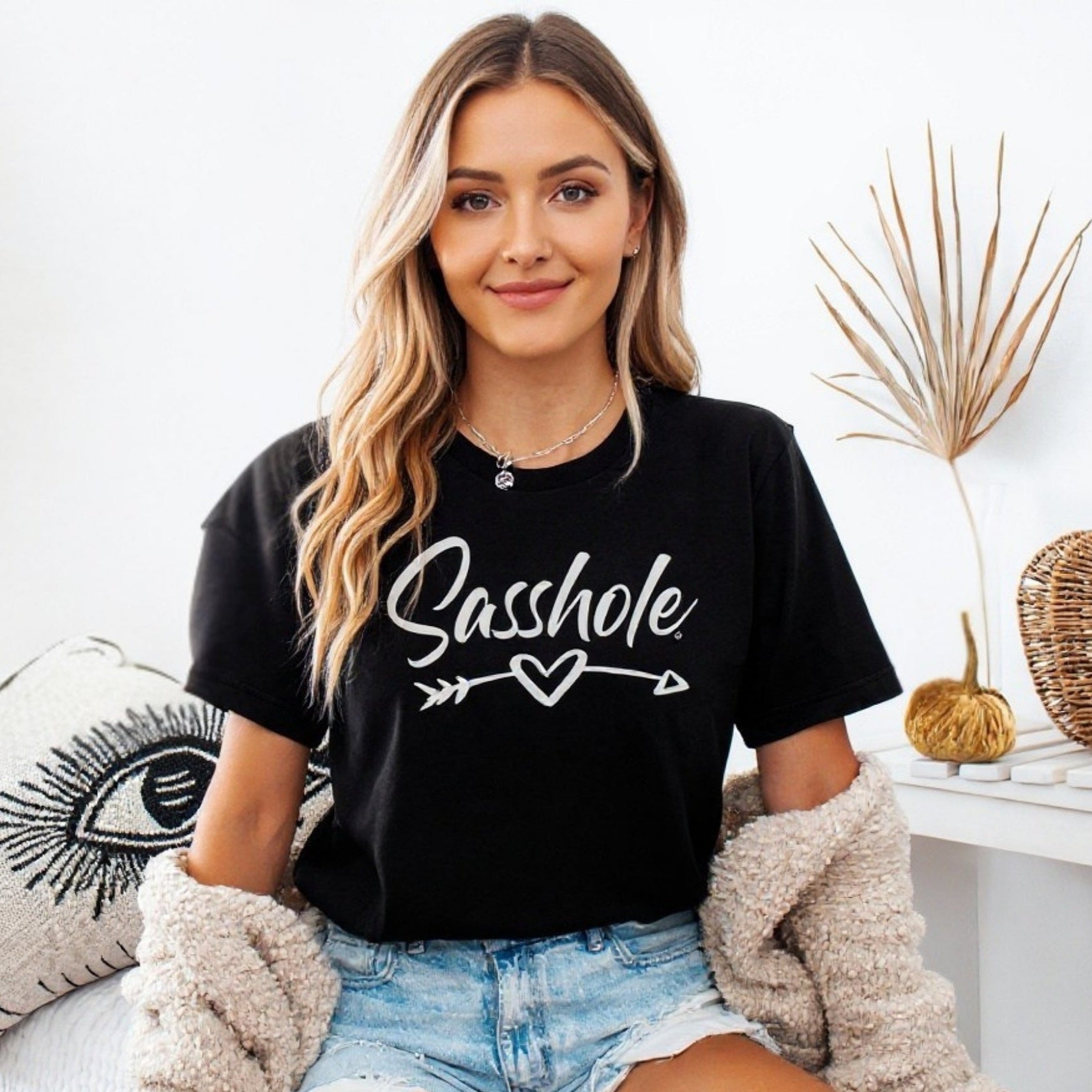 Woman wearing a black t-shirt with 'Sasshole' text, sitting on a couch.
