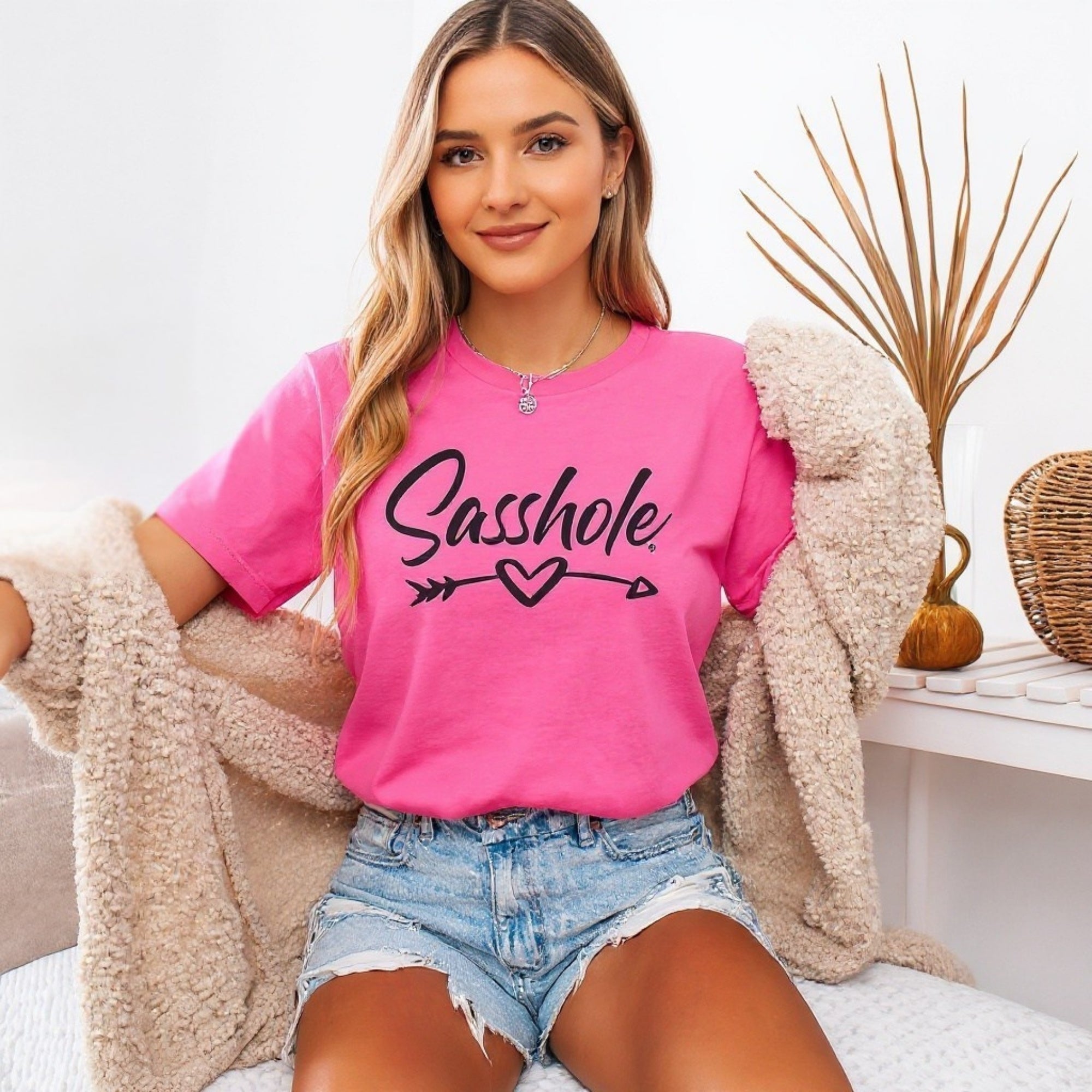 Image of Woman wearing a pink t-shirt with 'Sasshole' text, sitting on a couch.