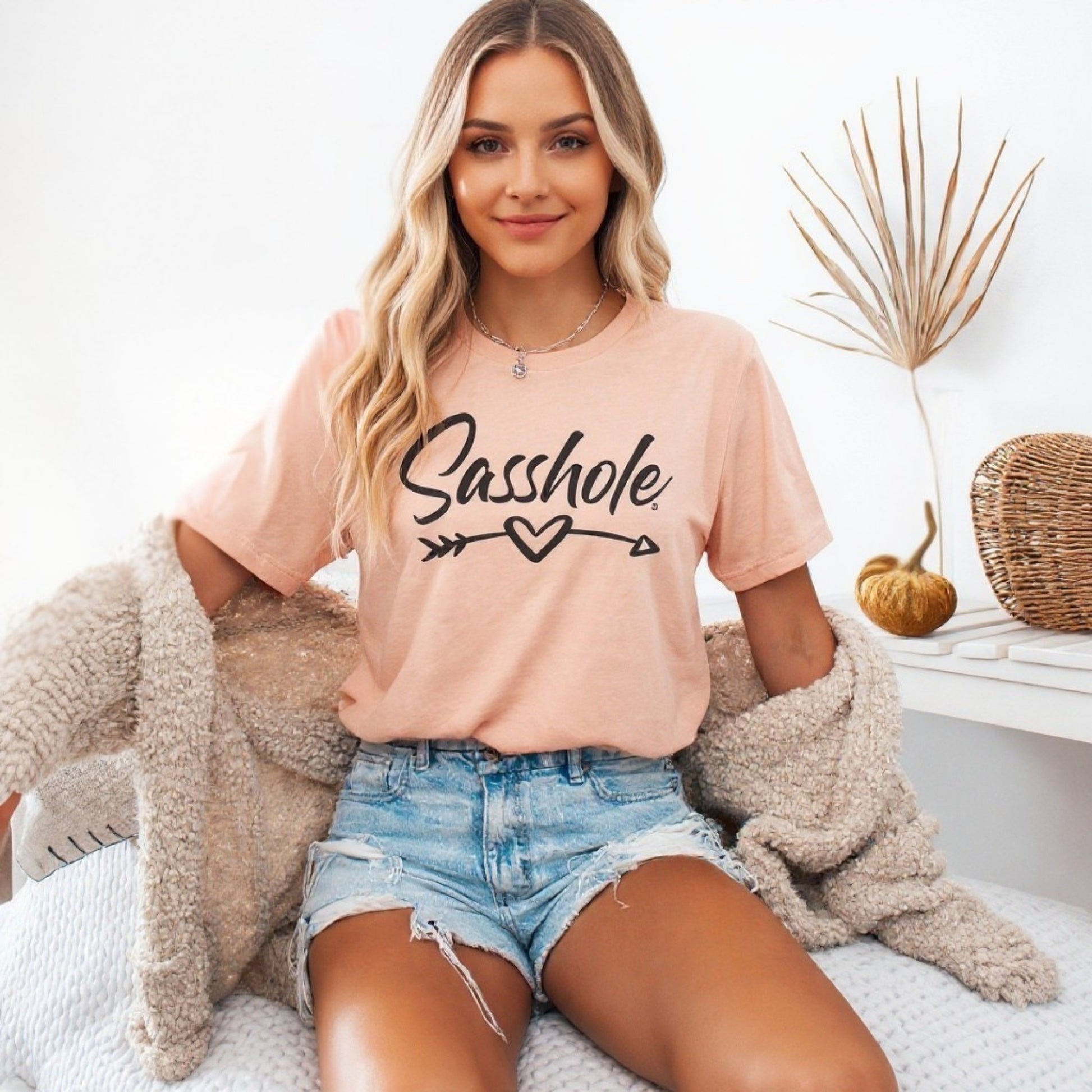 Woman wearing a pink t-shirt with 'Sasshole' text, sitting on a couch.