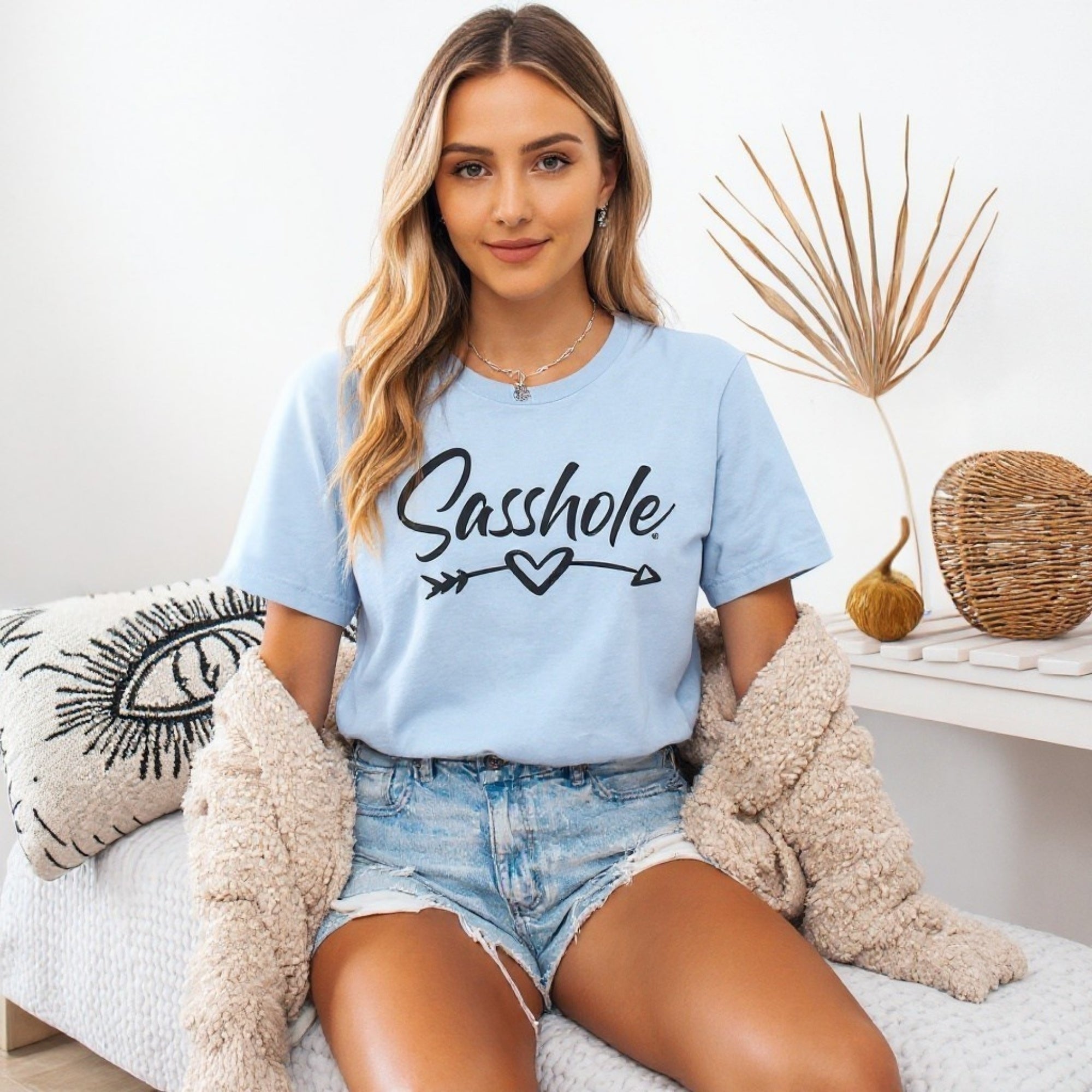 Image of Woman wearing a light blue t-shirt with 'Sasshole' text, sitting on a couch.