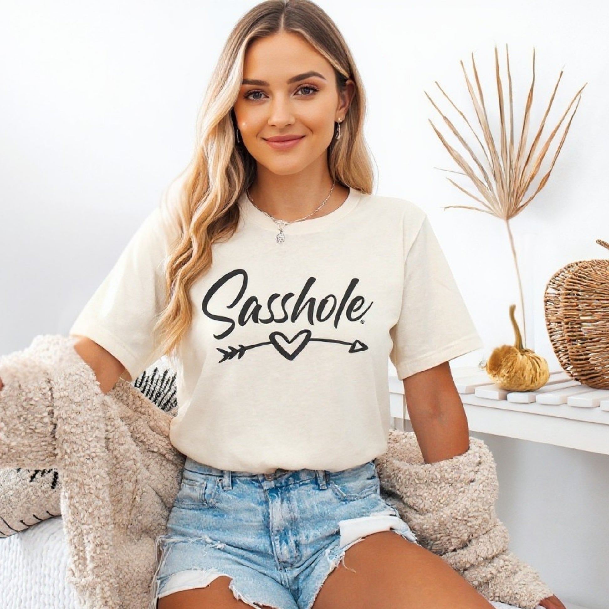 Woman wearing a natural t-shirt with 'Sasshole' text, sitting in a cozy room